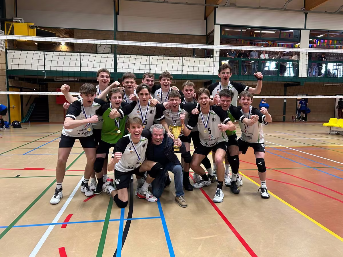 De U19 van Rembert balt de vuisten rond de Champions League-beker, met de coach geknield in het midden.