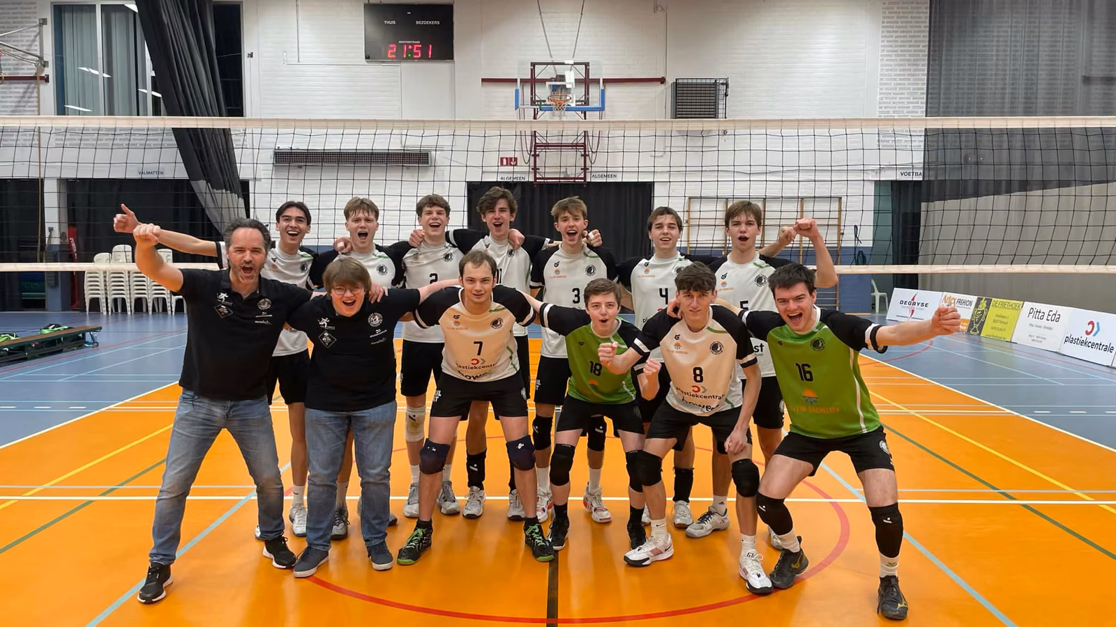 Spelers en coaches van Rembert juichen met gebalde vuisten in de sporthal na het behalen van de titel.