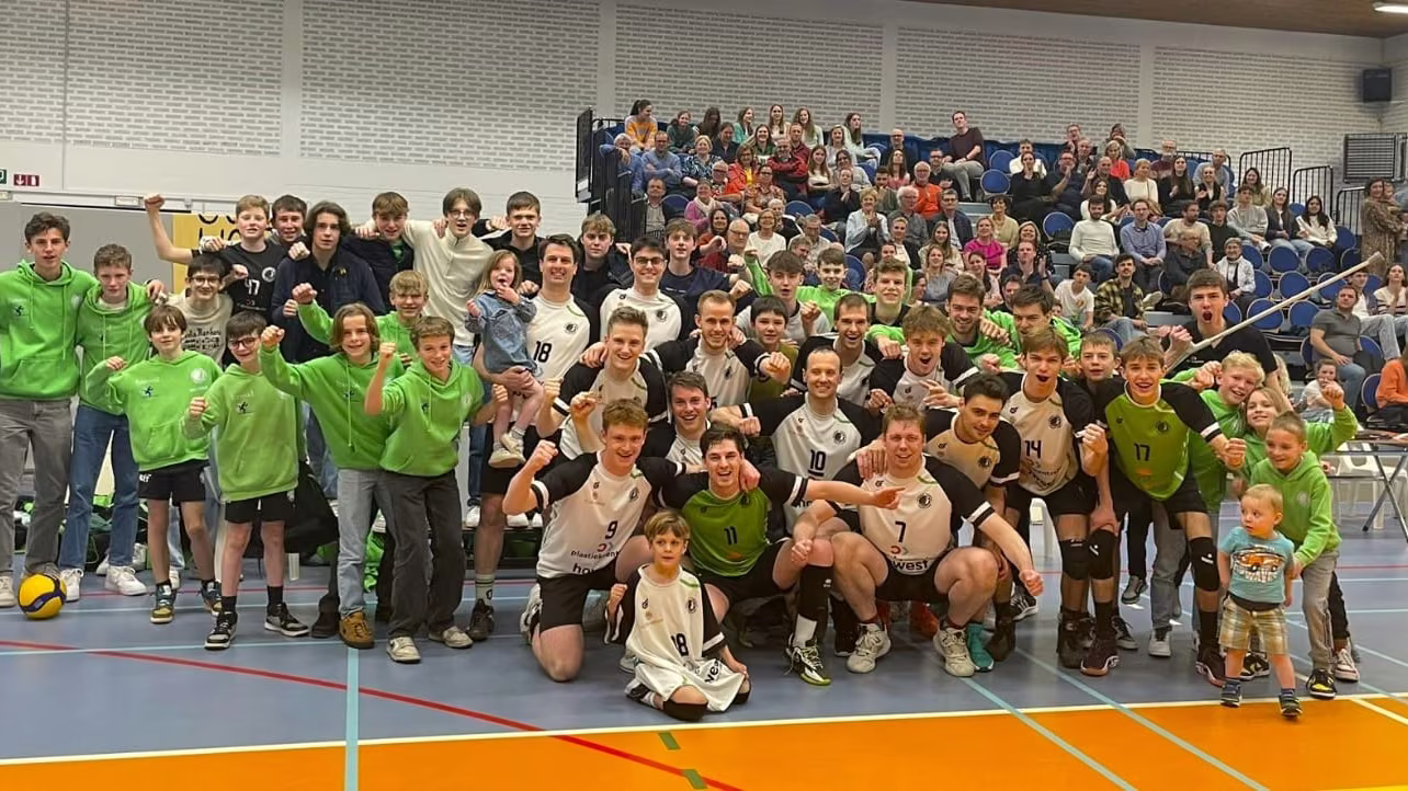 Seniorenspelers en jeugdspelers vieren samen op het veld, met een volle tribune supporters erachter