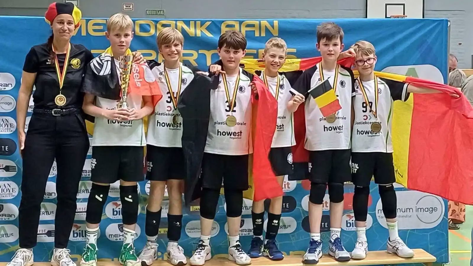 De U11-ploeg met medailles en Belgische vlaggen naast hun coach op het podium van het Belgisch Kampioenschap in Stekene